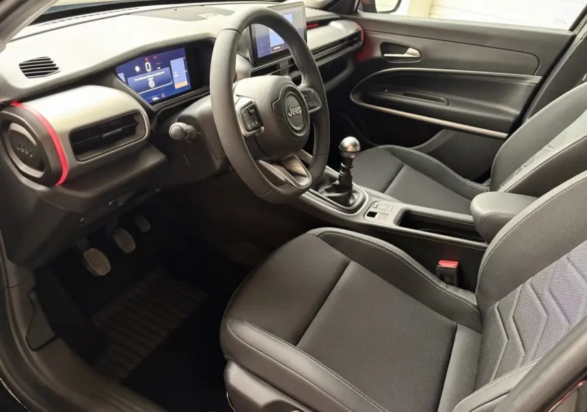 Intérieur Jeep Avenger 2025 vu côté conducteur, tableau de bord noir avec touches rouges et volant cuir multifonctions.