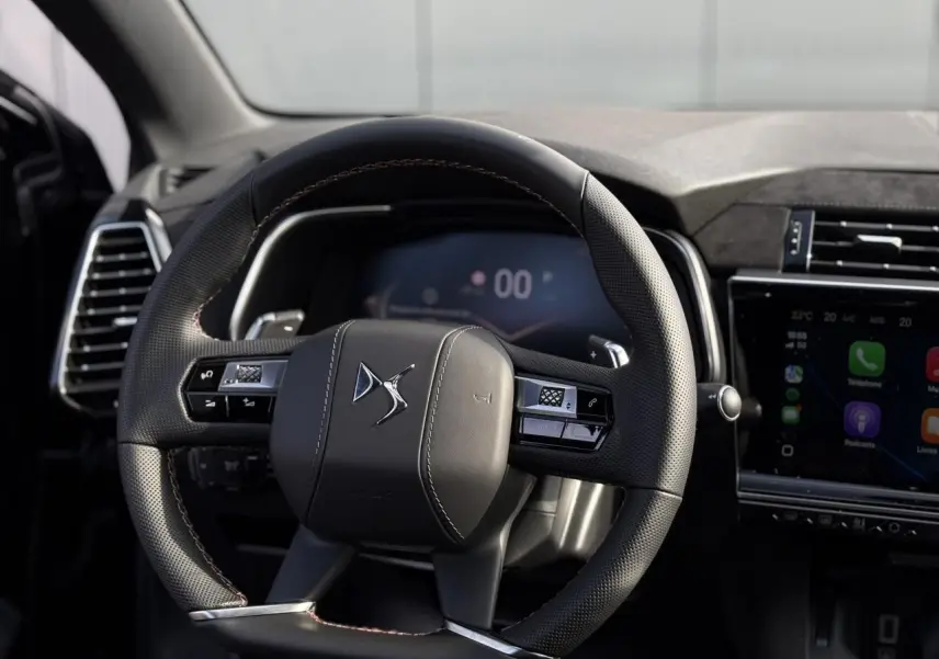 Volant en cuir noir perforé avec surpiqûres Carmin et Or du DS7 2025, tableau de bord et écran tactile visibles.