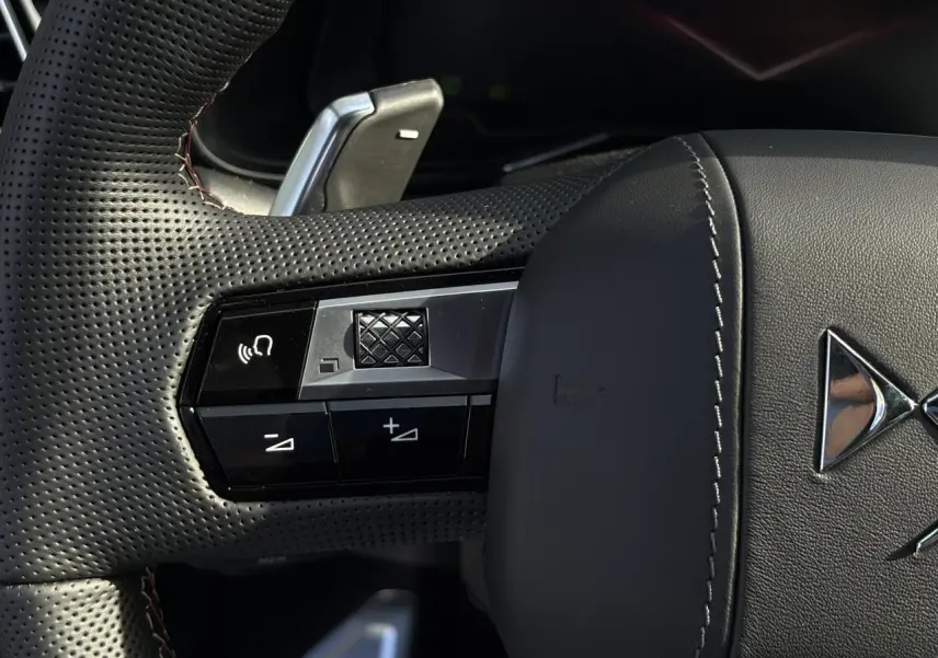 Gros plan sur le volant en cuir perforé noir avec surpiqûres Carmin et commandes multifonctions du DS7 2025.
