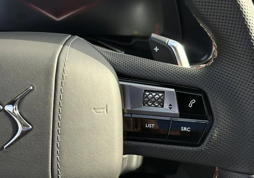 Gros plan sur le volant en cuir perforé noir avec surpiqûres rouges et commandes multifonctions du DS7 2025.