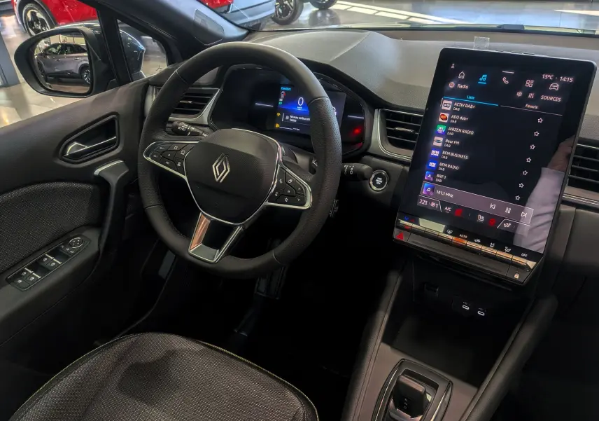 Vue intérieure côté conducteur du Renault Captur 2025, volant multifonction et grand écran tactile central allumé.