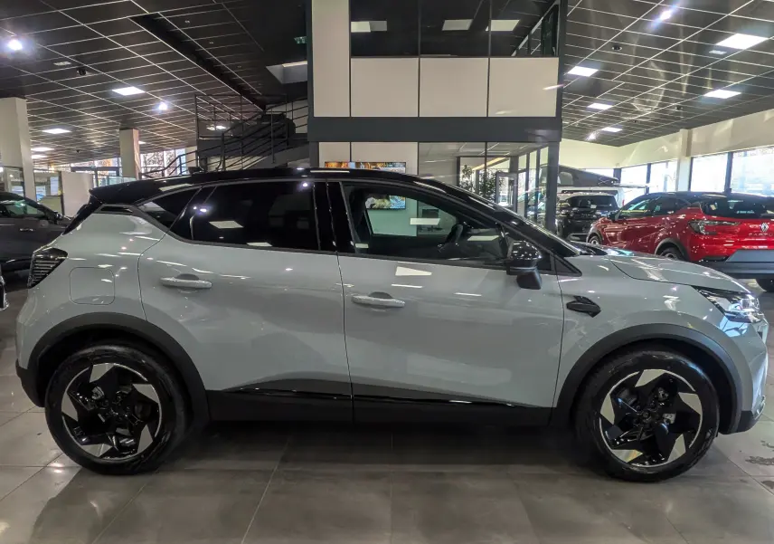 Profil côté gauche du Renault Captur 2025 gris Rafale avec toit noir et jantes noires bicolores en showroom.