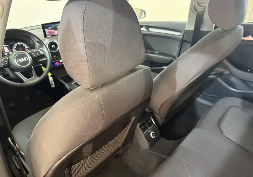 Vue intérieure arrière de l'Audi A3 2018, sièges tissu gris et tableau de bord avec écran navigation visible.