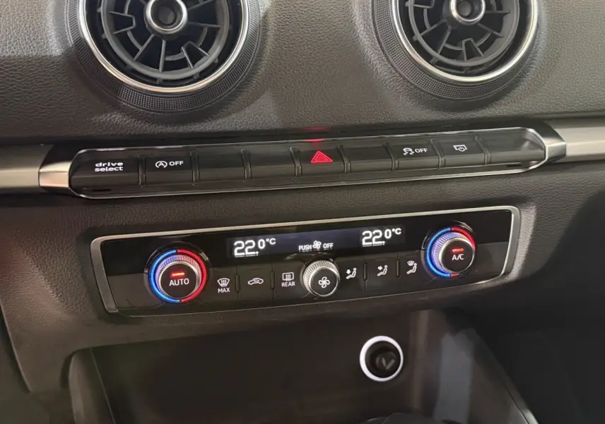 Détail de la console centrale de l'Audi A3 bleu, montrant la climatisation digitale bi-zone et les aérateurs ronds noirs.