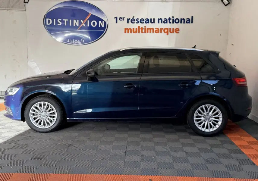 Profil côté gauche d'une Audi A3 2.0 TDI Business Line bleu foncé, avec jantes alliage et vitres teintées, en intérieur showroom.