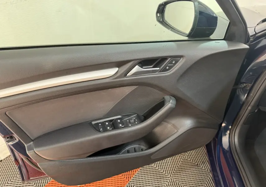 Vue rapprochée de la porte avant gauche bleu foncé d'une Audi A3 2018, avec commandes électriques et poignée noire.