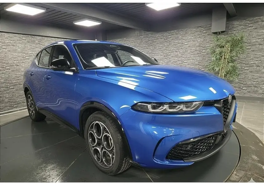 Vue 3/4 avant gauche d'un Alfa Romeo Tonale 2025 bleu métallisé avec jantes alliage et calandre noire distinctive.
