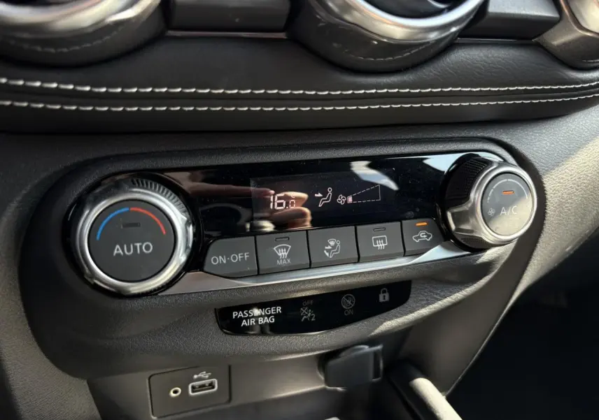 Vue rapprochée de la console centrale du Nissan Juke 2024 gris, montrant les commandes de climatisation automatique et port USB.