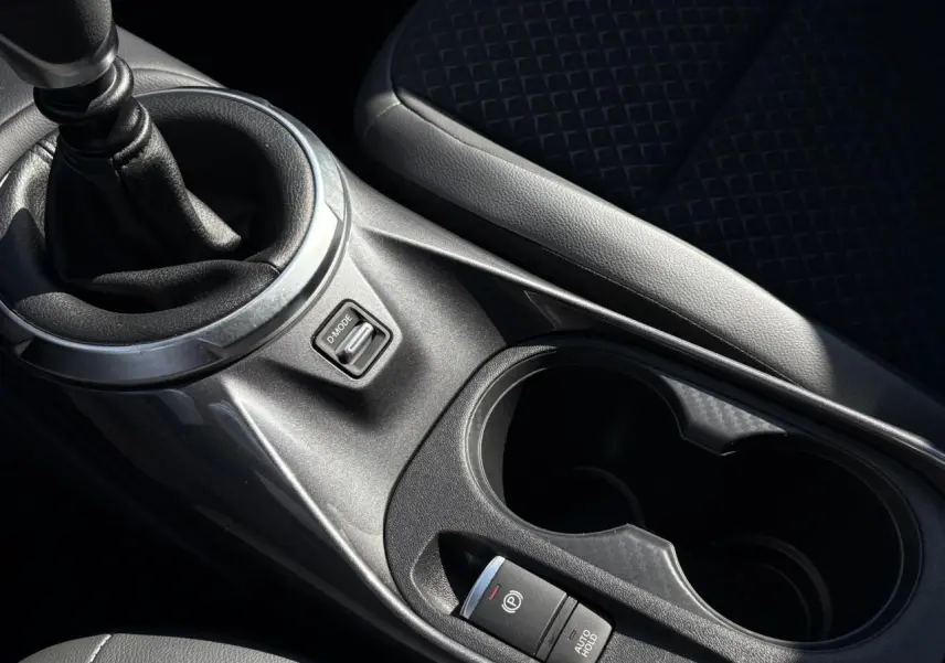 Gros plan sur la console centrale du Nissan Juke 2024 avec levier de vitesses manuel et bouton frein à main électrique.