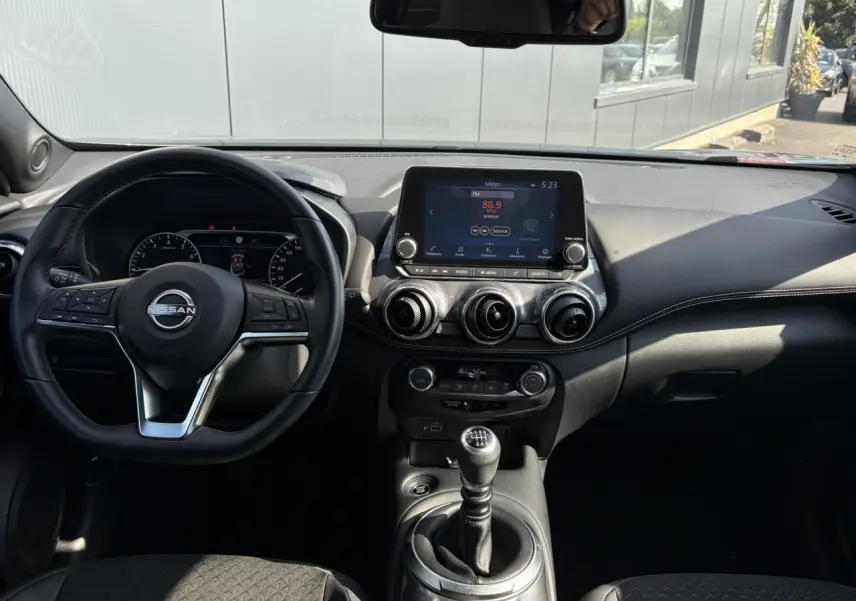 Vue intérieure du tableau de bord du Nissan Juke 2024 avec volant multifonction, écran tactile et levier de vitesses manuel.