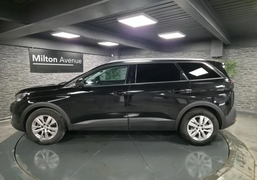 Profil côté gauche d'un Peugeot 5008 noir métallisé 2021 dans un showroom avec jantes alliage 17 pouces.