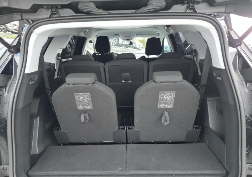 Vue arrière du coffre ouvert d'un Peugeot 5008 noir montrant les sièges escamotables du troisième rang relevés.