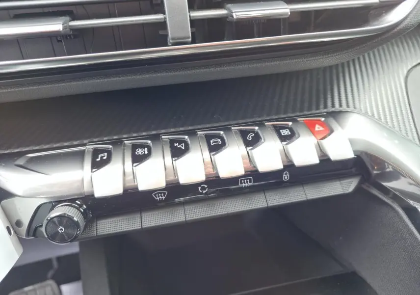 Gros plan sur la console centrale du Peugeot 5008 noir 2021, mettant en valeur les commandes chromées et le décor carbone.