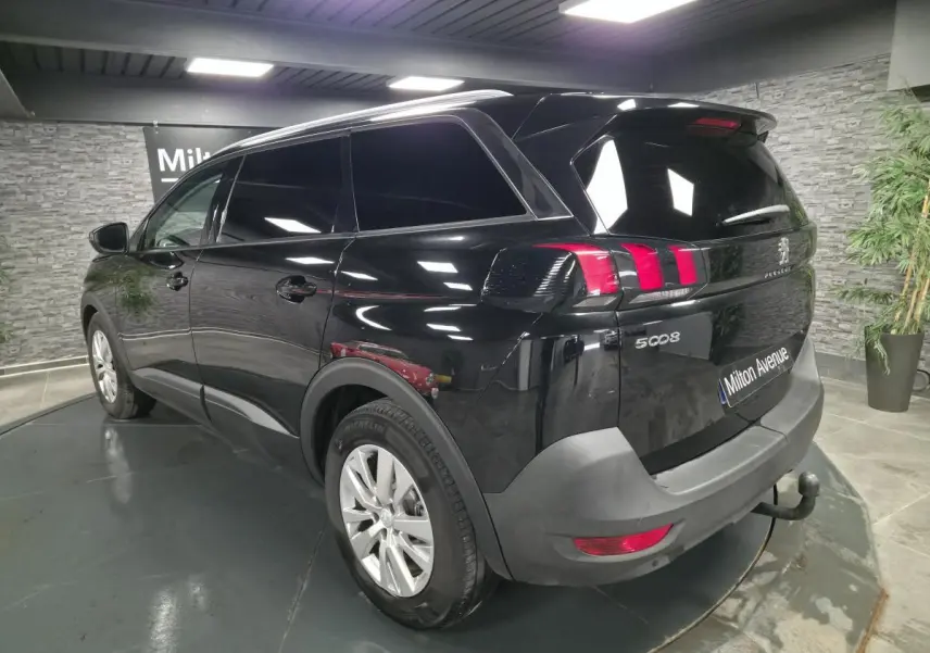 Vue 3/4 arrière droite du Peugeot 5008 noir avec attelage et jantes alliage dans un showroom intérieur.