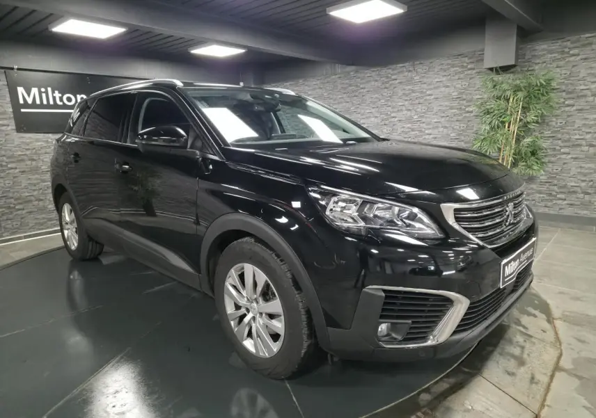 Peugeot 5008 noir vue 3/4 avant droit en intérieur avec calandre chromée et jantes alliage 17 pouces.
