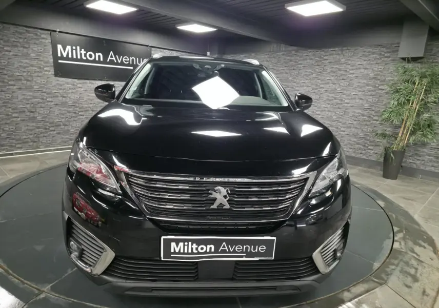 Vue frontale d'un Peugeot 5008 noir avec calandre chromée et feux LED, en intérieur sur plateau tournant.