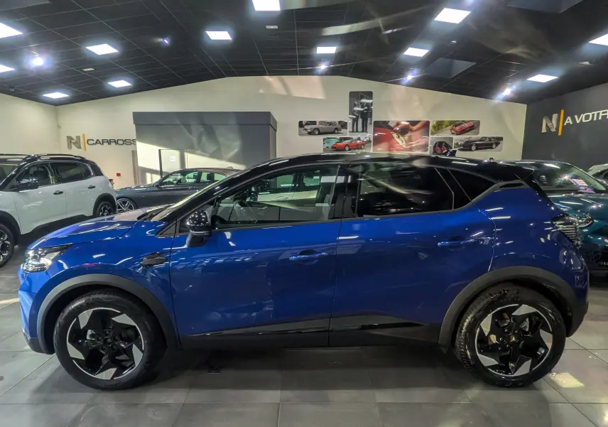 Renault Captur 2025 bleu Iron avec toit noir vu de profil côté gauche en intérieur showroom.