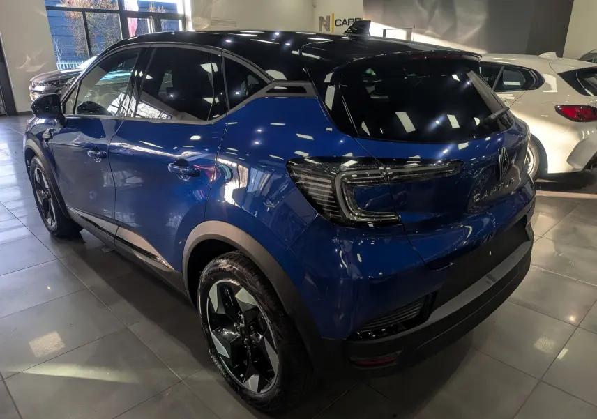 Vue 3/4 arrière droite du Renault Captur 2025 bleu Iron avec toit noir et feux arrière LED en intérieur showroom.