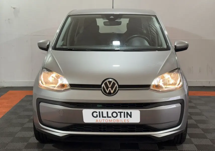 Vue avant d'une Volkswagen Up gris foncé avec phares allumés sur sol intérieur à damier noir et orange.