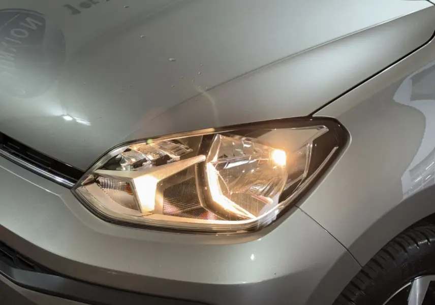 Gros plan sur le phare avant droit allumé d'une Volkswagen Up gris foncé, avec partie du capot visible.