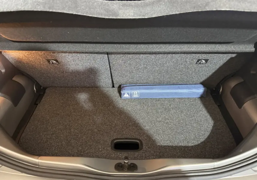 Coffre ouvert d’une Volkswagen Up gris foncé, vue de dessus montrant la moquette et un kit de sécurité bleu.