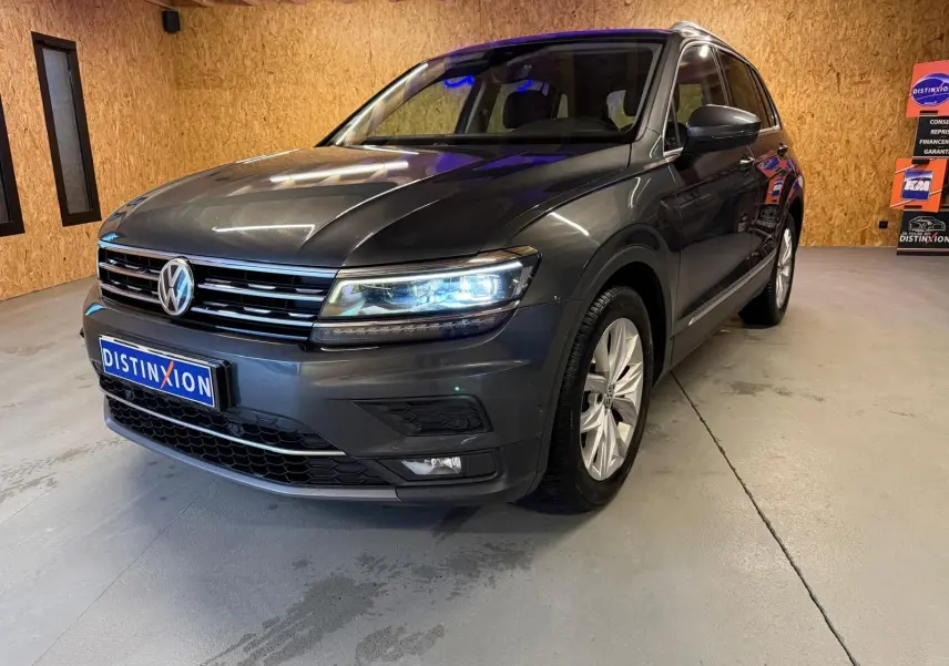 Volkswagen Tiguan gris 3/4 avant droit avec phares allumés dans un garage à murs en bois.