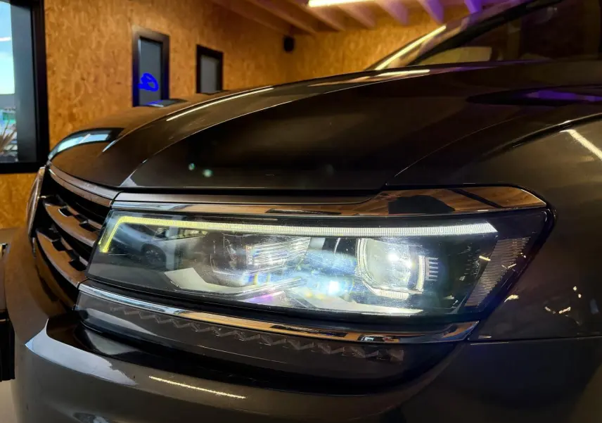 Gros plan sur le phare avant droit du Volkswagen Tiguan gris, mettant en valeur les LED et la calandre chromée.