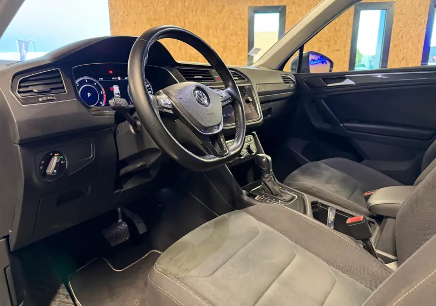 Vue intérieure côté conducteur du Volkswagen Tiguan gris, volant cuir multifonctions et console centrale avec boîte auto.
