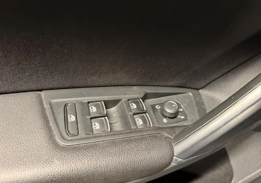 Gros plan sur les commandes des vitres électriques et rétroviseurs rabattables côté gauche d’un Volkswagen Tiguan gris.