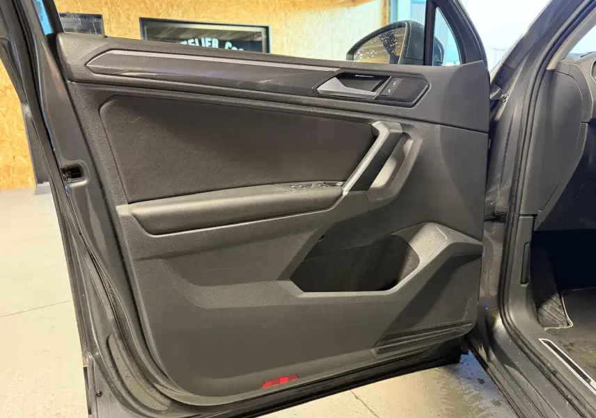 Vue intérieure de la porte avant gauche grise du Volkswagen Tiguan 2018 avec commandes de vitres et poignée argentée.