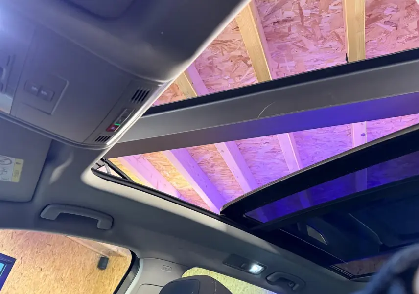 Vue intérieure du toit ouvrant panoramique ouvert du Volkswagen Tiguan gris, avec éclairage intérieur et plafond en bois visible.