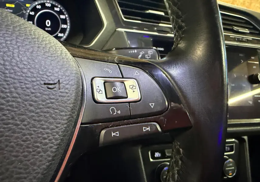 Gros plan sur le volant cuir noir du Volkswagen Tiguan 2018 avec commandes multifonctions et tableau de bord numérique.