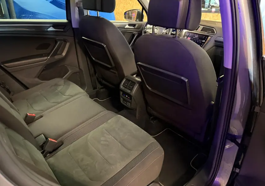 Vue intérieure arrière côté droit du Volkswagen Tiguan gris, montrant la banquette et les sièges avant avec prises et aérateurs centraux.