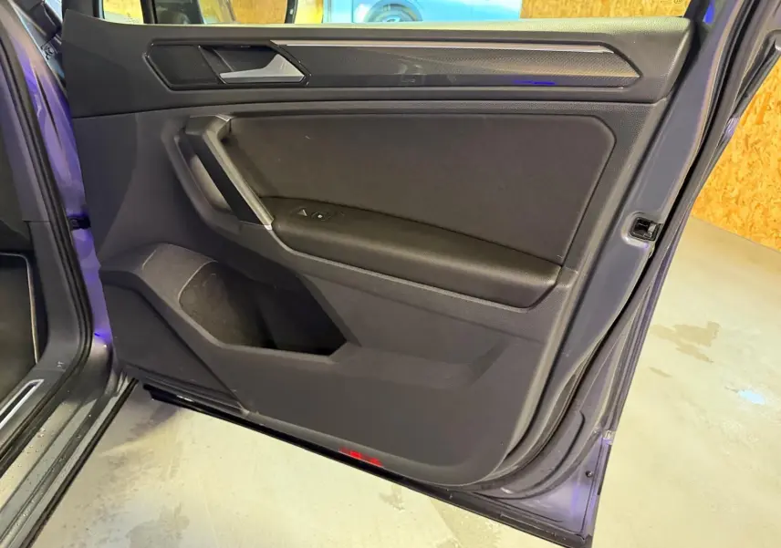 Vue intérieure côté gauche de la porte avant d'un Volkswagen Tiguan gris, avec garniture noire et poignée intégrée.