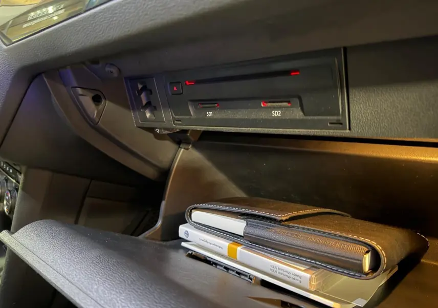 Gros plan intérieur sur la boîte à gants ouverte du Volkswagen Tiguan gris, montrant des manuels et lecteurs SD intégrés.