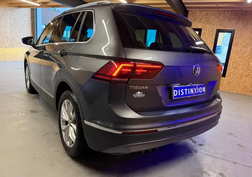 Vue 3/4 arrière droite d'un Volkswagen Tiguan gris avec feux arrière allumés dans un garage.