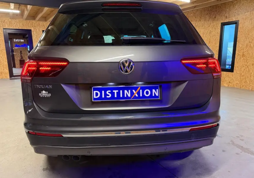 Vue arrière d'un Volkswagen Tiguan gris avec feux allumés dans un garage en bois.