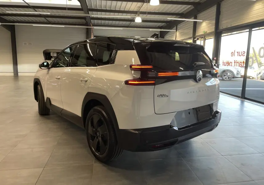 Vue 3/4 arrière droite du Citroën C5 Aircross blanc Okenite avec toit noir et feux arrière LED distinctifs en intérieur showroom.