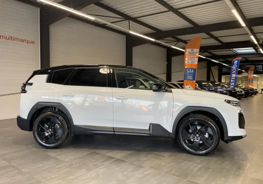 Vue latérale droite du Citroën C5 Aircross blanc Okenite avec toit noir et jantes alliage noires en intérieur showroom.