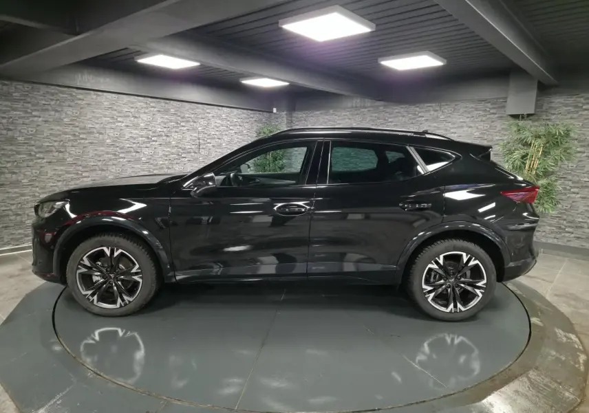 Vue de profil côté gauche d'un CUPRA Formentor noir avec jantes alliage 18'' usinées dans un showroom intérieur.