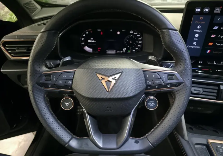 Volant sport noir perforé avec logo CUPRA cuivré, vue frontale du poste de conduite et tableau de bord digital.