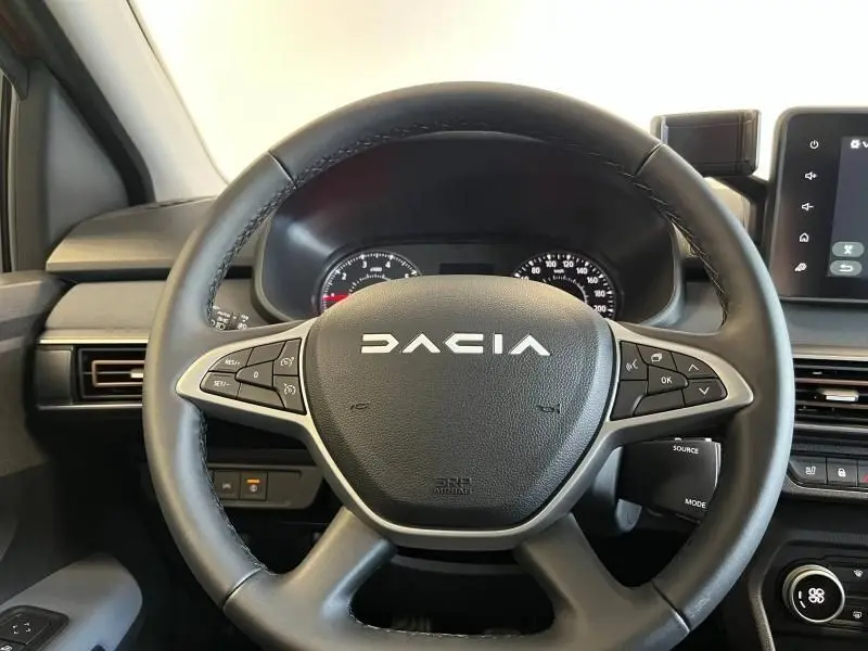 Volant noir avec logo DACIA en vue frontale, tableau de bord et écran tactile partiellement visibles à droite