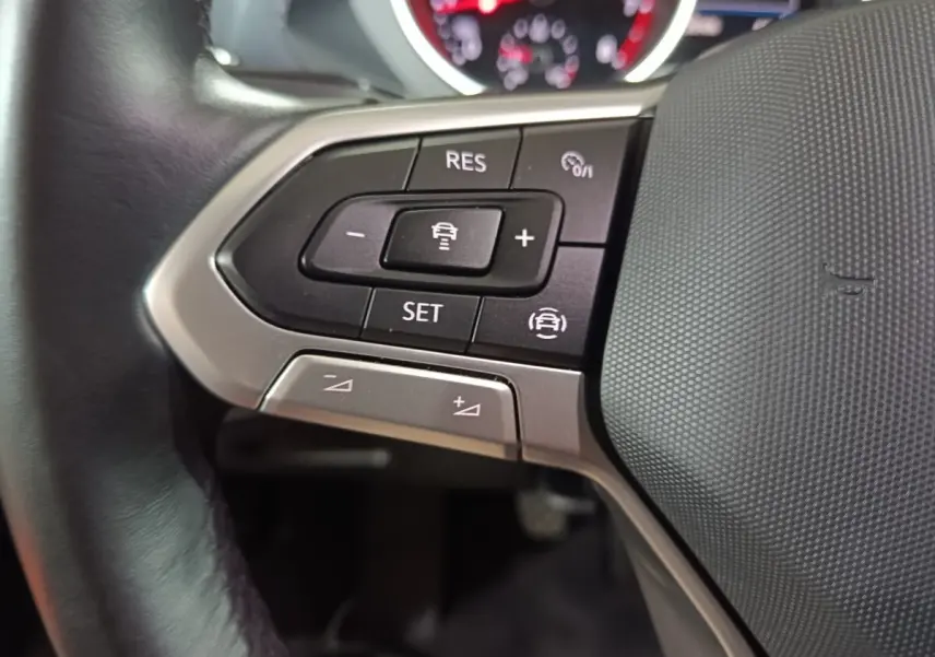 Gros plan sur le côté gauche du volant cuir du Volkswagen Tiguan bleu, avec commandes multifonctions visibles.