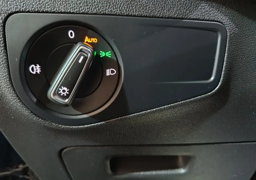 Gros plan sur le bouton de commande des phares du Volkswagen Tiguan 2021, intérieur noir avec réglage automatique activé.