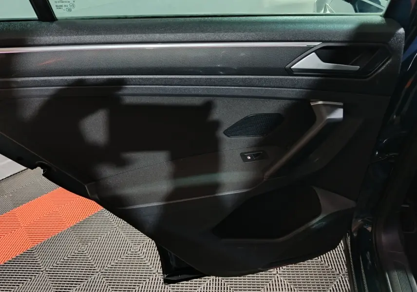 Vue intérieure de la porte arrière droite du Volkswagen Tiguan bleu, avec poignée et commande de vitre électrique.