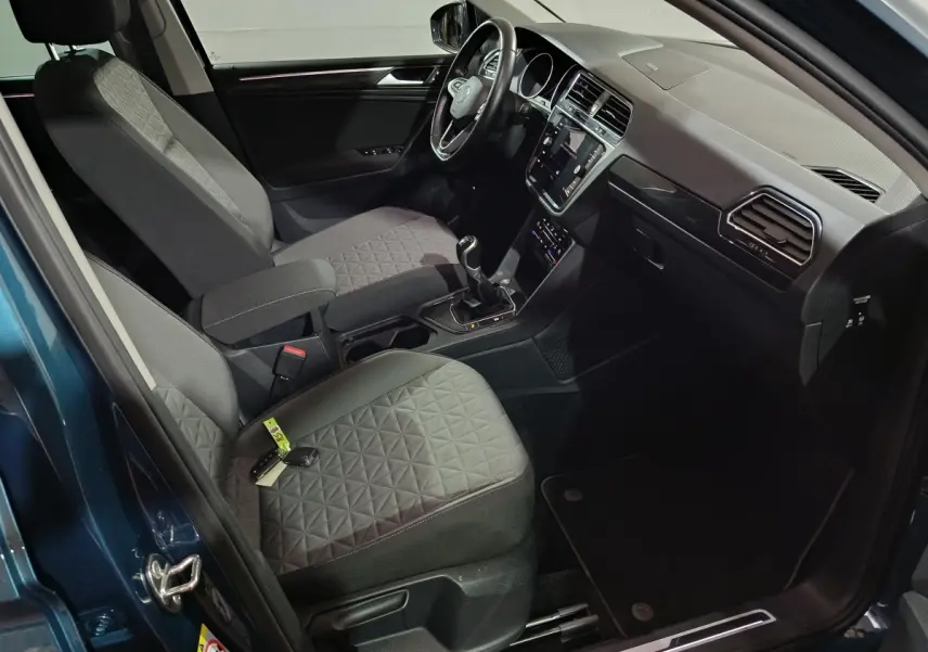 Intérieur avant droit du Volkswagen Tiguan bleu 2021, volant cuir multifonctions, sièges tissu gris à motifs géométriques.