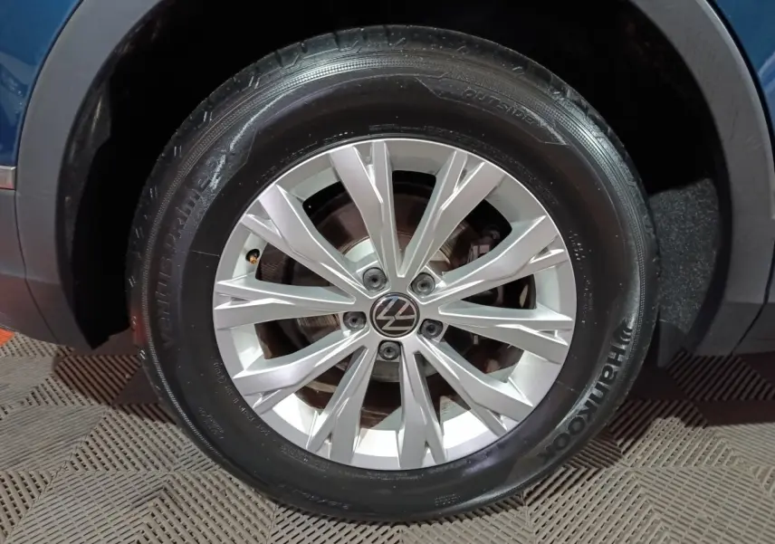 Gros plan sur la roue avant gauche d’un Volkswagen Tiguan bleu, avec jante alliage argentée et logo VW au centre.