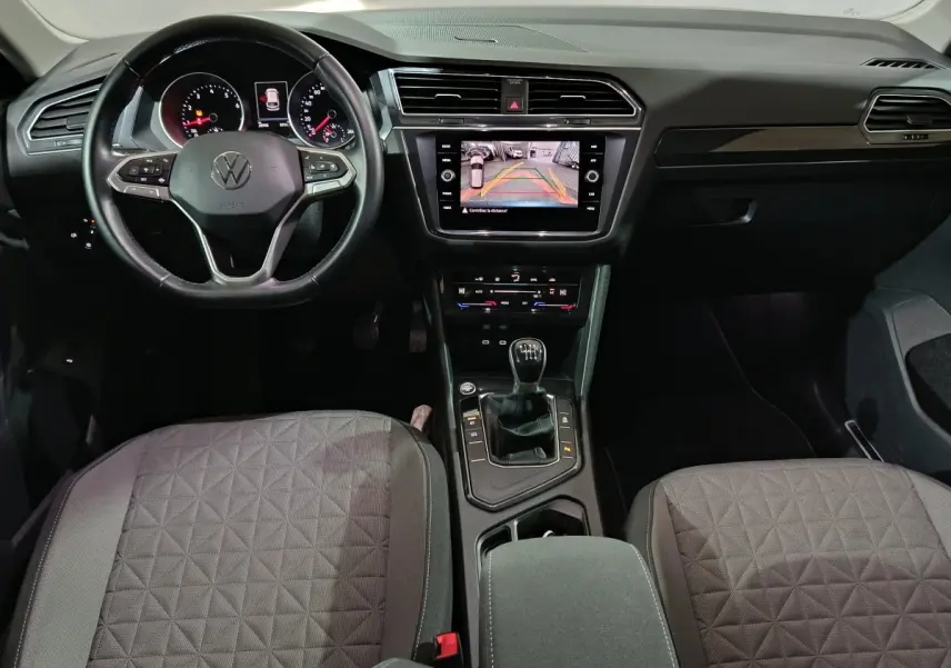 Vue intérieure avant du Volkswagen Tiguan 2021 avec volant cuir multifonctions, écran tactile et levier de vitesses manuel.