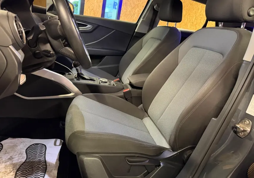 Vue intérieure côté conducteur de l'Audi Q2 gris, montrant les sièges bi-ton et la console centrale avec levier de vitesse automatique.