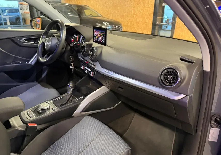 Vue intérieure côté passager de l'Audi Q2 gris, mettant en valeur le tableau de bord et la console centrale avec écran GPS.
